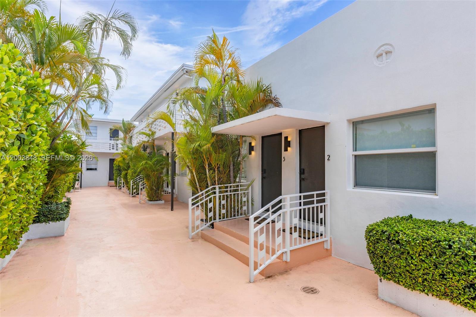 An exterior view of a white apartment building with palm trees and numbered unit doors — 7320 Byron Ave, Miami Beach FL 33141, MIAMI BEACH, FL