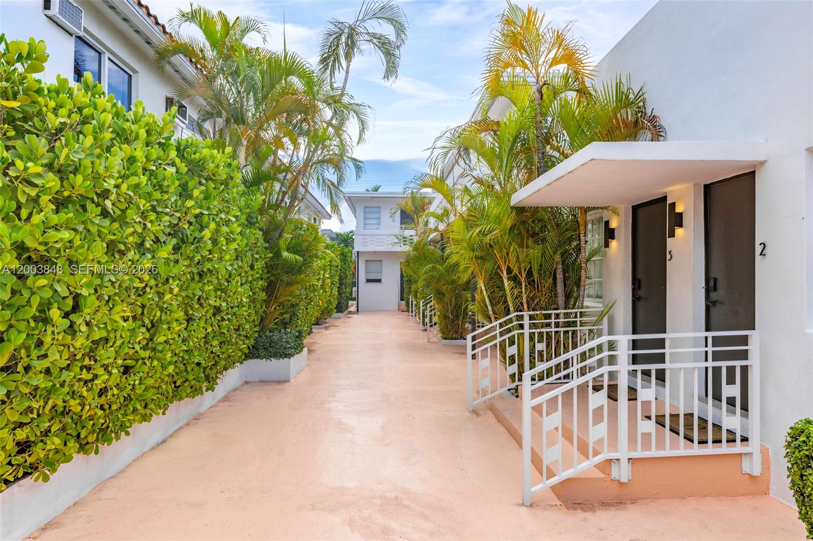 A walkway leads between two white buildings with palm trees and a hedge — 7320 Byron Ave, Miami Beach FL 33141, MIAMI BEACH, FL