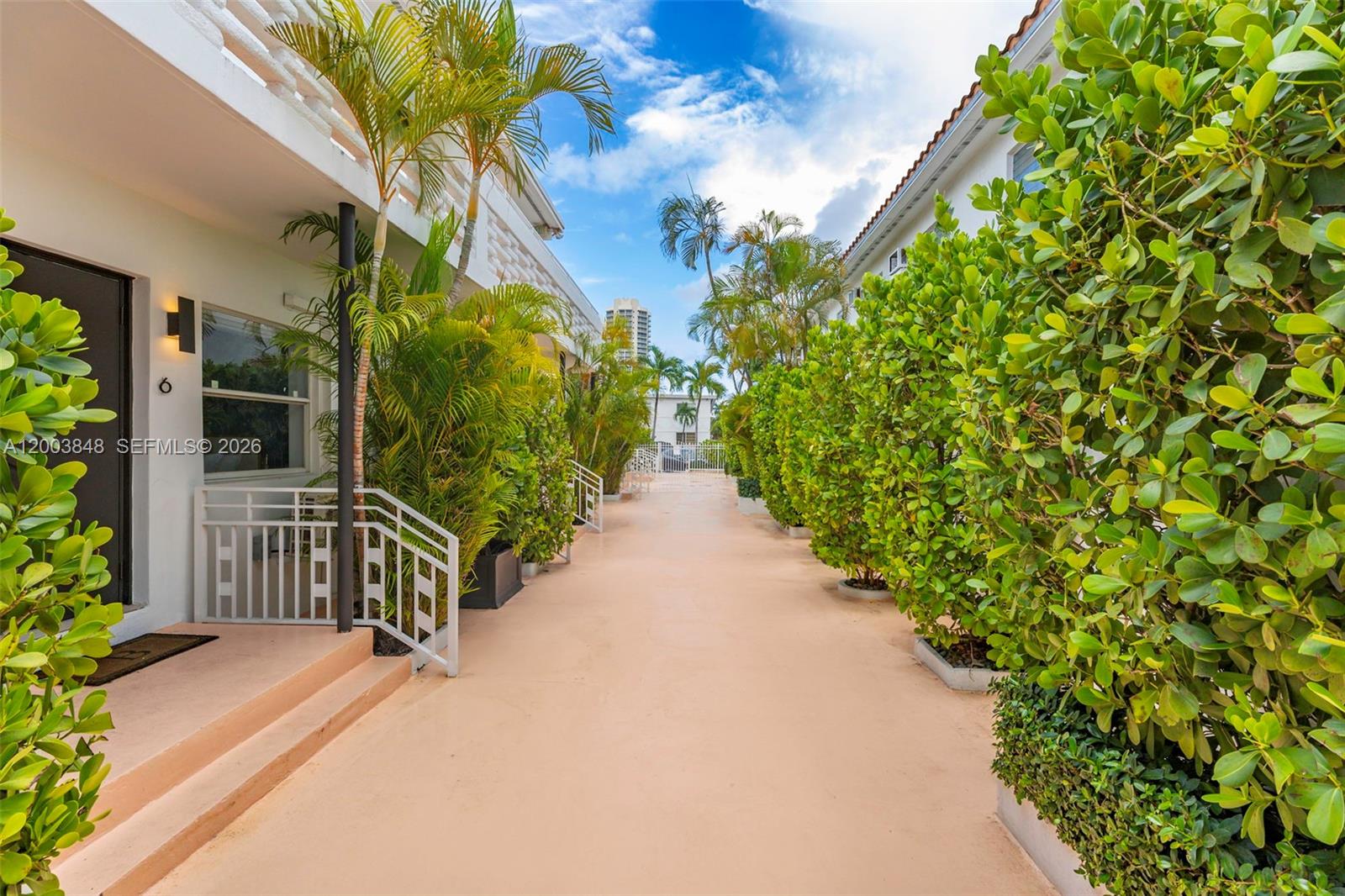 An outdoor walkway between two residential buildings features lush landscaping and a light-colored floor — 7320 Byron Ave, Miami Beach FL 33141, MIAMI BEACH, FL