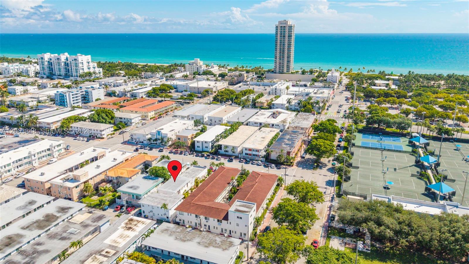This aerial view shows a multi-story residential building with a red roof near tennis courts — 7320 Byron Ave, Miami Beach FL 33141, MIAMI BEACH, FL