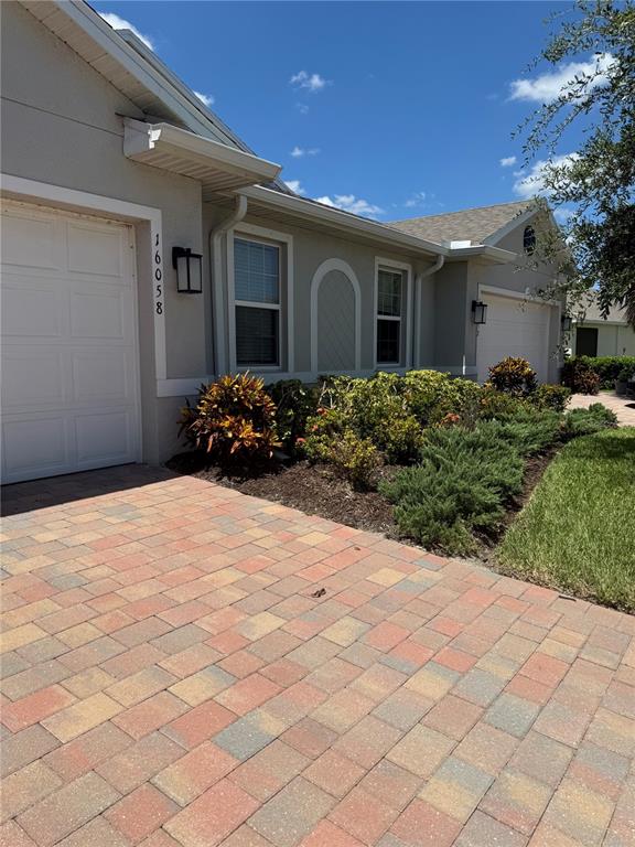 A beige house exterior features a paved driveway, a garage, and landscaped front garden beds — 16058 BRIDLE RIDGE STREET, PORT CHARLOTTE, FL