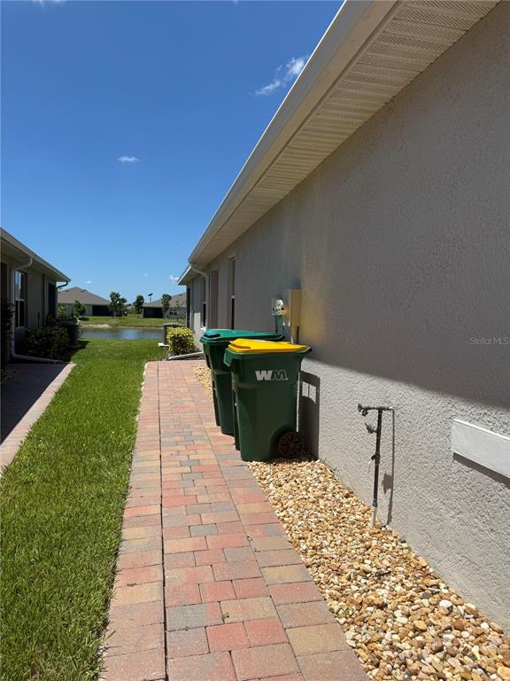 A brick walkway runs along the side of a house next to two trash bins — 16058 BRIDLE RIDGE STREET, PORT CHARLOTTE, FL