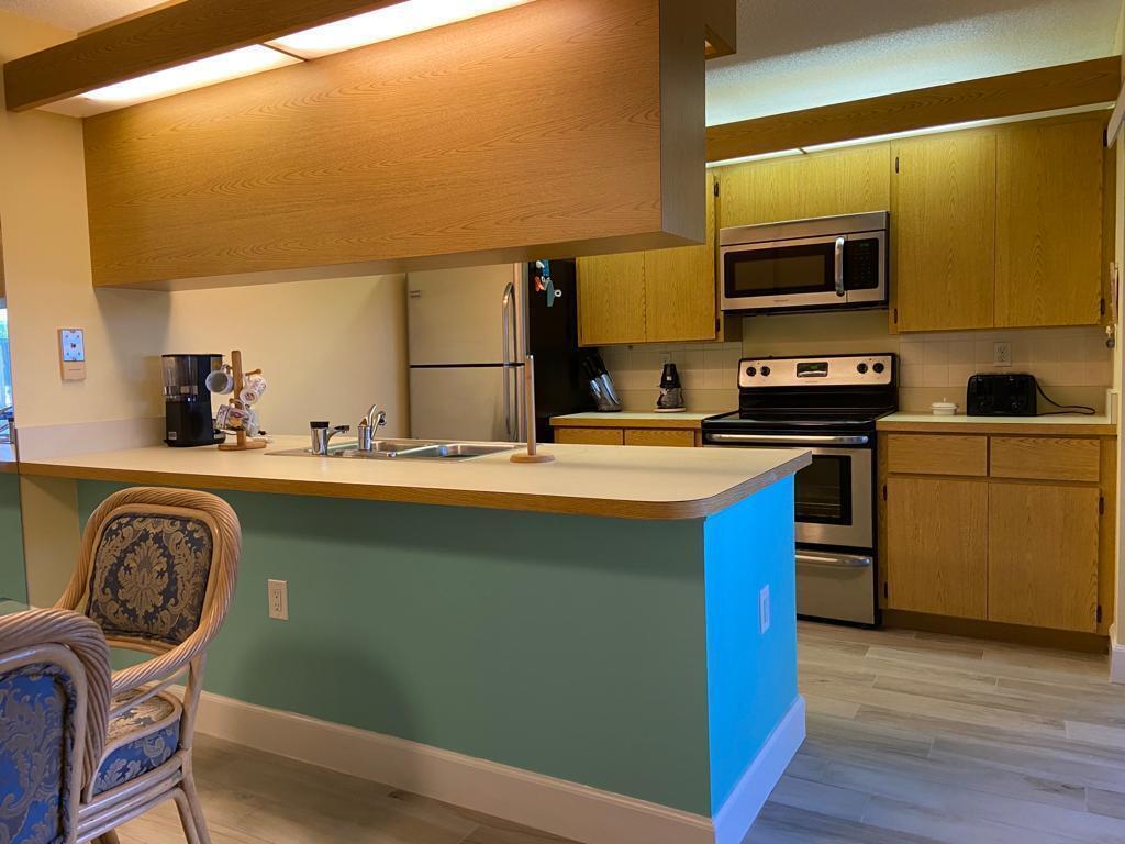 A kitchen features light wood cabinets, stainless steel appliances, and a teal-painted breakfast bar — 8010 80th Way, West Palm Beach FL 33407, WEST PALM BEACH, FL