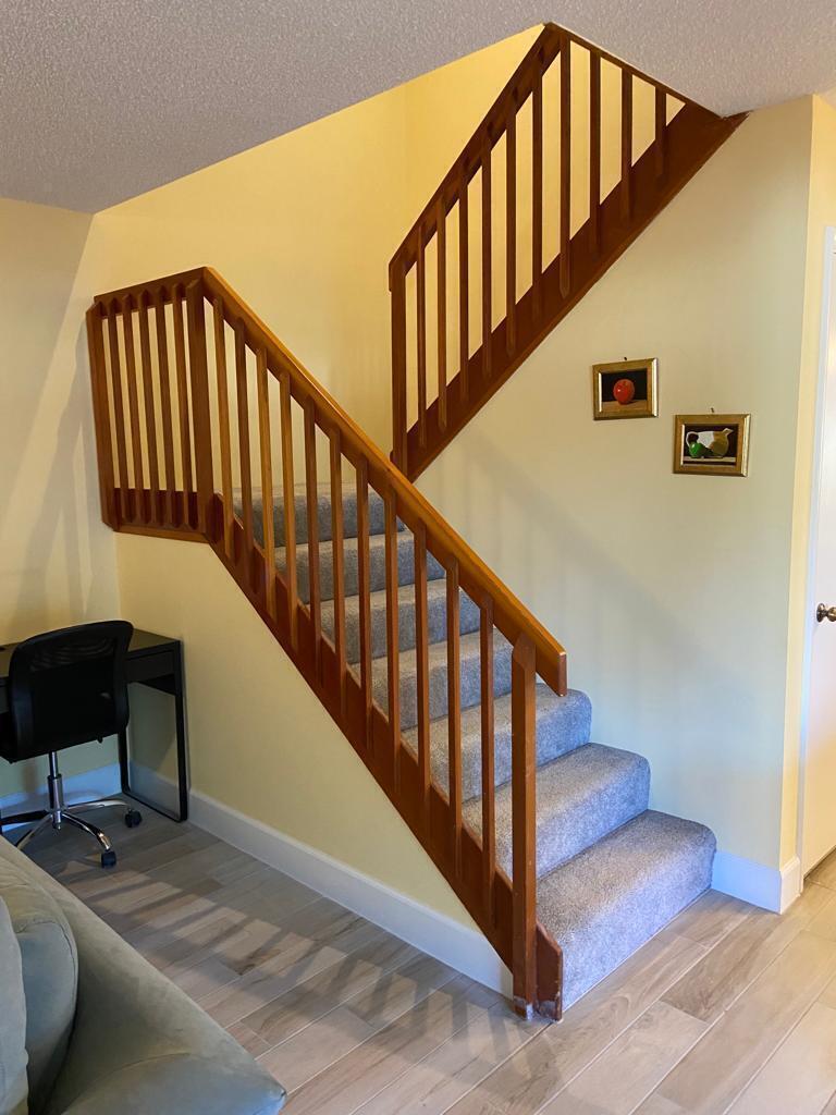 A carpeted staircase with wooden railings ascends against a yellow wall in a room — 8010 80th Way, West Palm Beach FL 33407, WEST PALM BEACH, FL