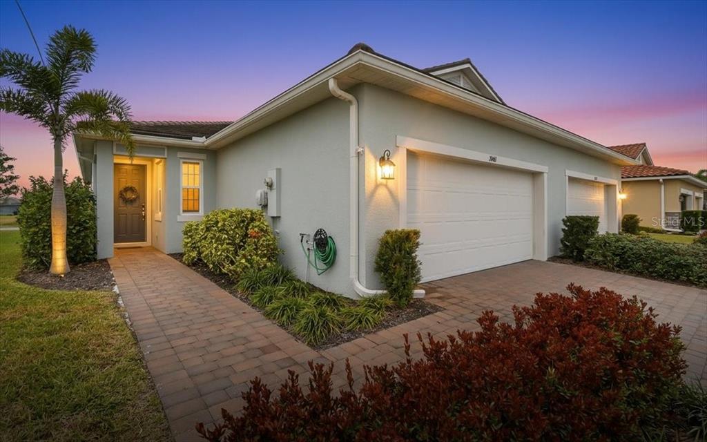 A single-story house with a paved walkway, a two-car garage, and a palm tree — 20461 GALILEO PLACE, VENICE, FL