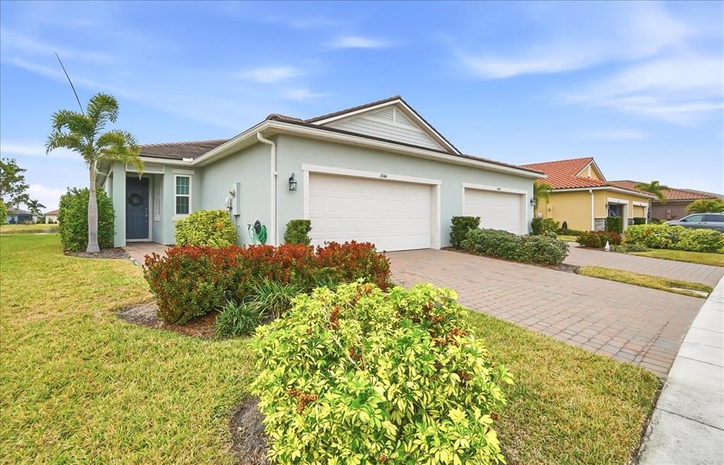 A light green single-story house with a two-car garage and a brick paver driveway — 20461 GALILEO PLACE, VENICE, FL