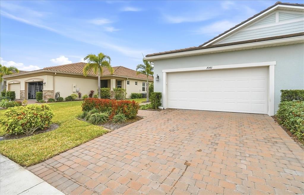 A paved driveway leads to the garage of a light-colored house with a tiled roof — 20461 GALILEO PLACE, VENICE, FL