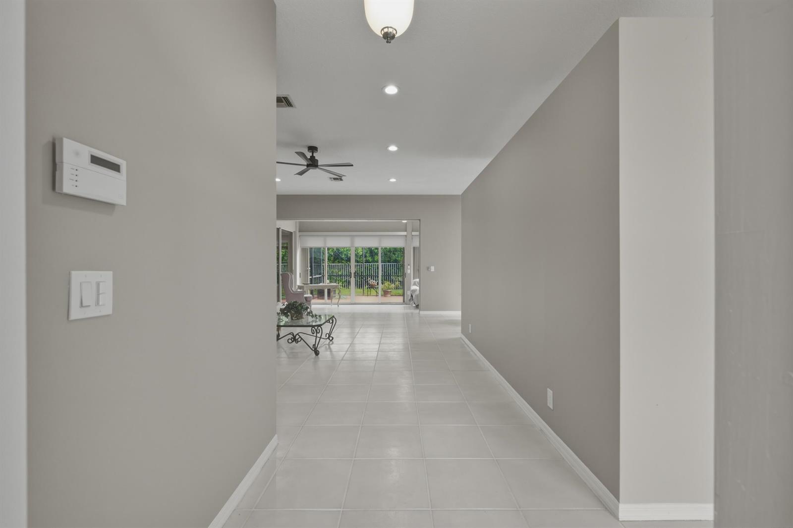 A hallway with light tile flooring leads toward a living area with sliding glass doors — 10827 La Salinas Circle, Boca Raton FL 33428, BOCA RATON, FL