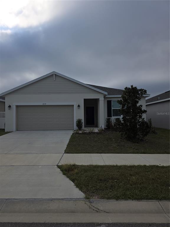 A single-story suburban house with a beige exterior, a two-car garage, and a front lawn — 1838 BLUE LAGOON CIRCLE, MASCOTTE, FL
