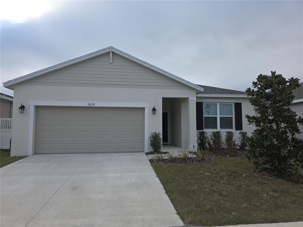 A single-story house with a beige stucco exterior, a two-car garage, and a front entrance — 1838 BLUE LAGOON CIRCLE, MASCOTTE, FL