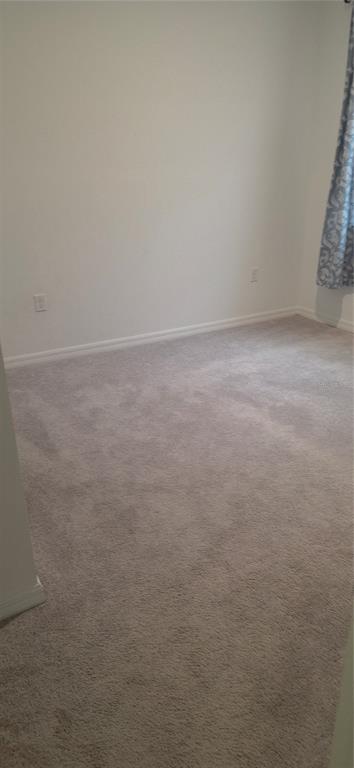 An empty bedroom features neutral walls, beige carpeting, and a blue patterned curtain — 1838 BLUE LAGOON CIRCLE, MASCOTTE, FL