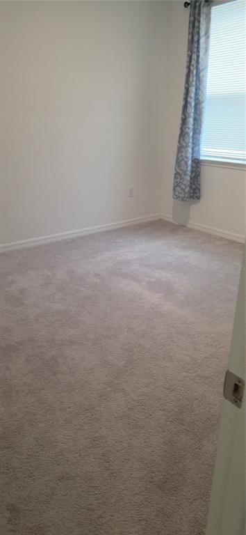 An empty bedroom features beige wall-to-wall carpeting, white walls, and a window with patterned curtains — 1838 BLUE LAGOON CIRCLE, MASCOTTE, FL
