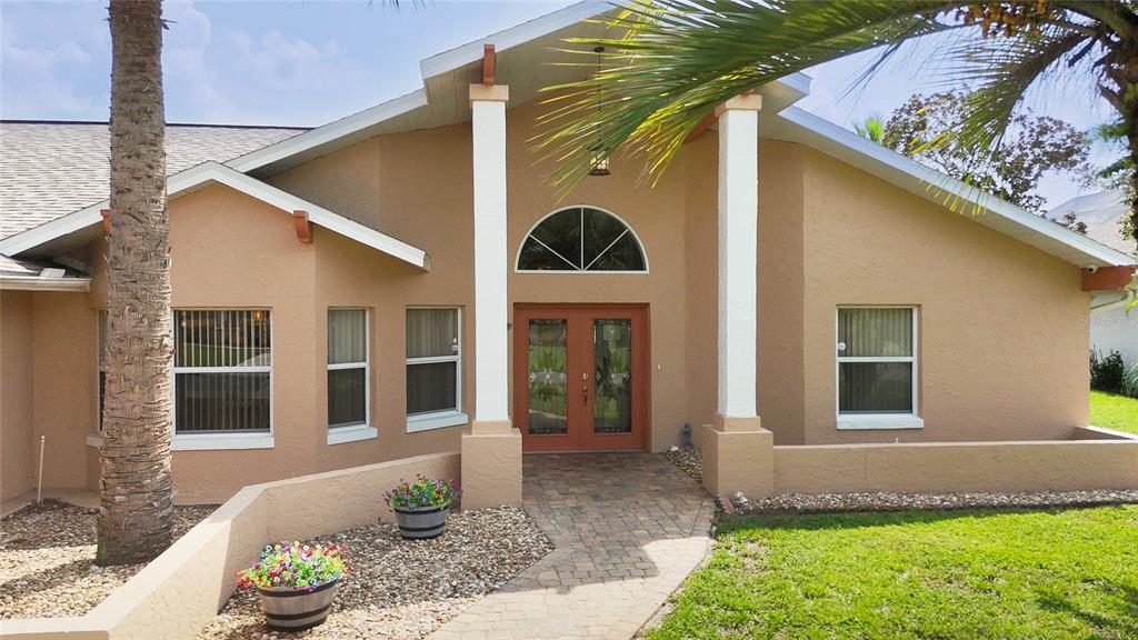 The exterior of a tan house features a stone walkway leading to double front doors — 38 WESTMOUNT LANE, PALM COAST, FL