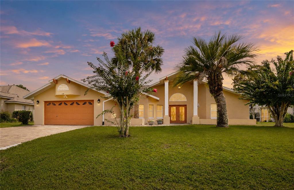 A single-story house with a tan stucco exterior, a two-car garage, and two palm trees — 38 WESTMOUNT LANE, PALM COAST, FL