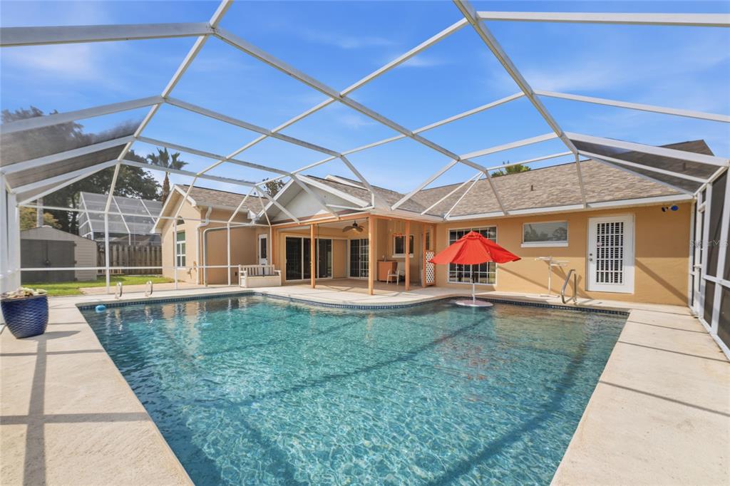 A swimming pool with a red umbrella sits inside a screened-in patio behind a house — 38 WESTMOUNT LANE, PALM COAST, FL