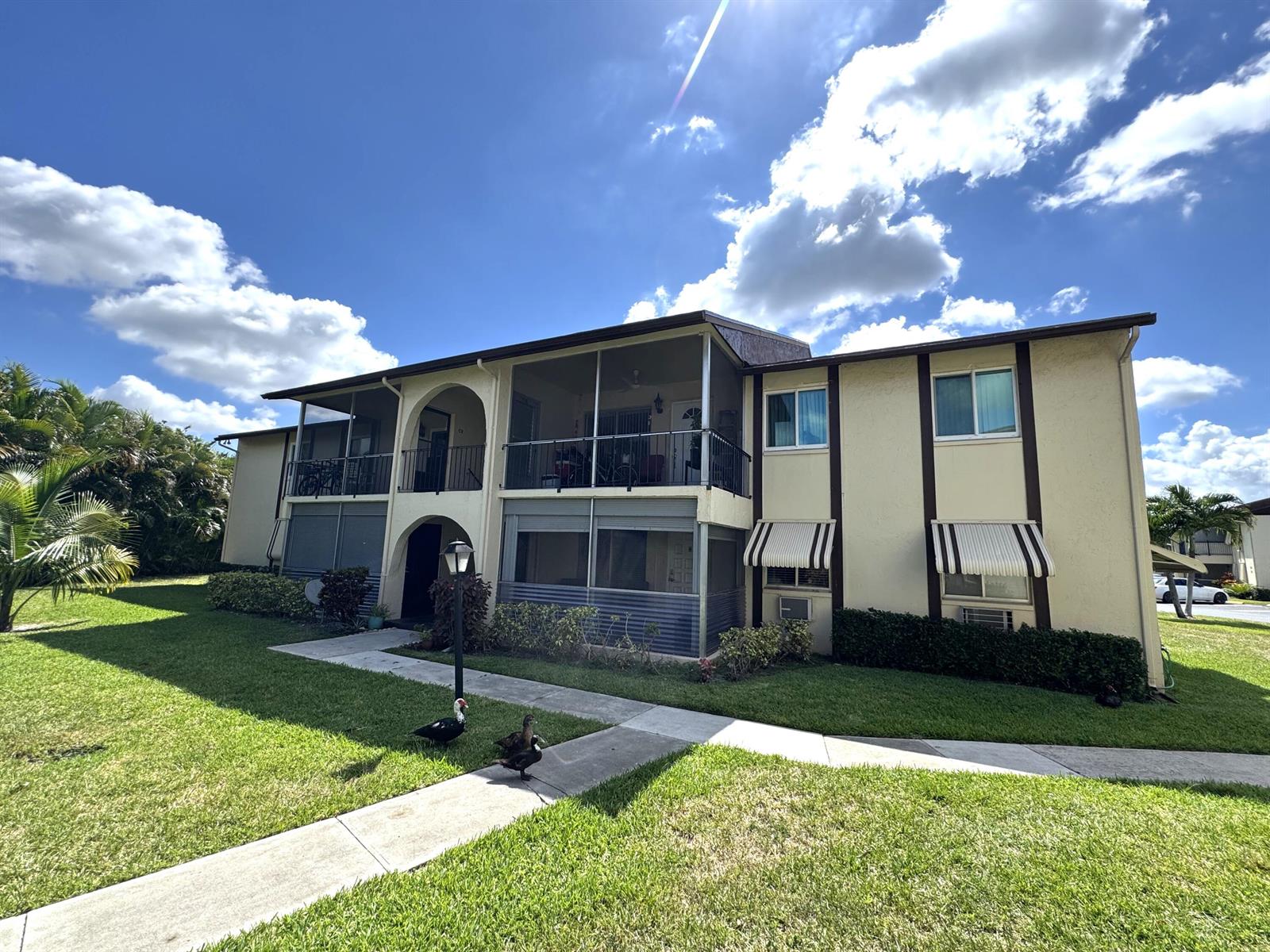 A two-story apartment building with screened balconies and striped awnings sits on a grassy lawn — 5817 La Pinata Boulevard # 1, FL 33463, FL