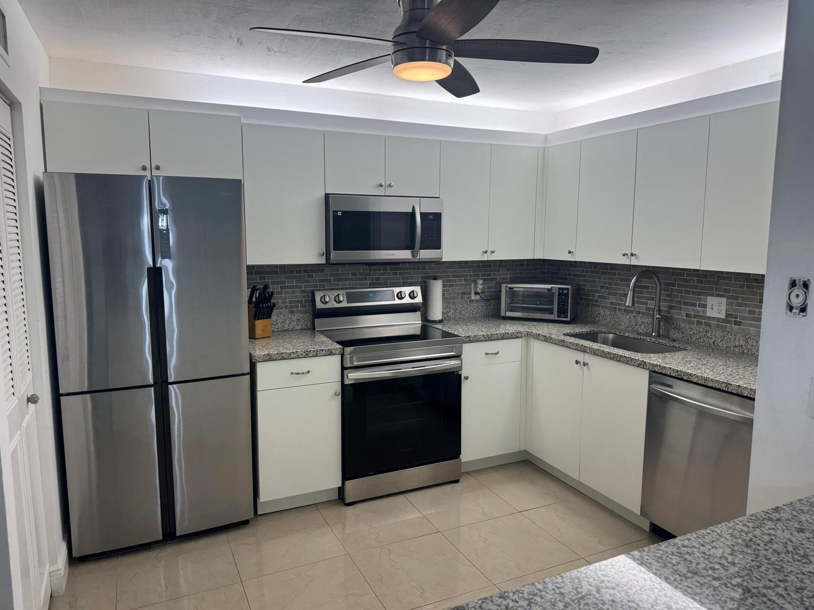 A kitchen featuring white cabinets, stainless steel appliances, granite countertops, and a gray tiled backsplash — 5817 La Pinata Boulevard # 1, FL 33463, FL