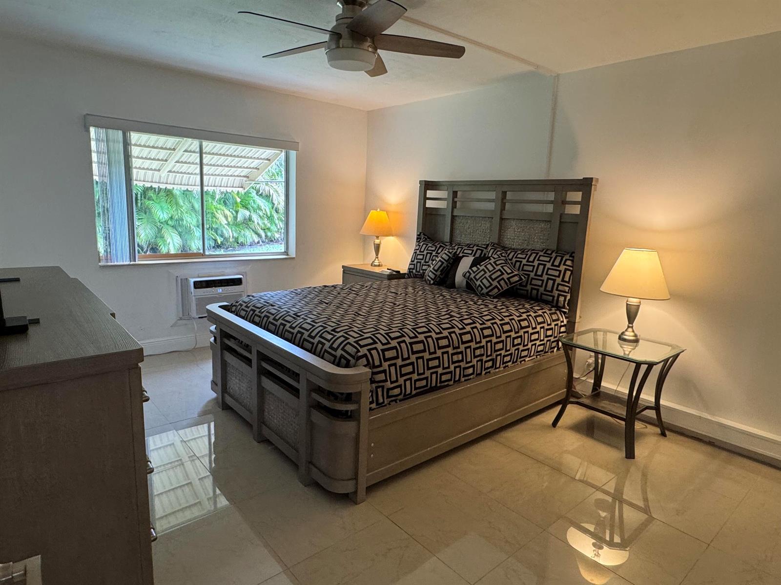 A bedroom features a patterned bed, two nightstands with lamps, a ceiling fan, and tile flooring — 5817 La Pinata Boulevard # 1, FL 33463, FL