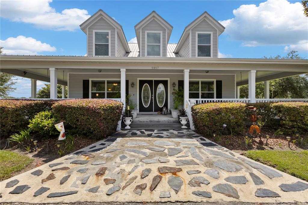 A gray house features a wraparound porch, three dormer windows, and a stone walkway — 9897 NW 160 AVENUE, MORRISTON, FL