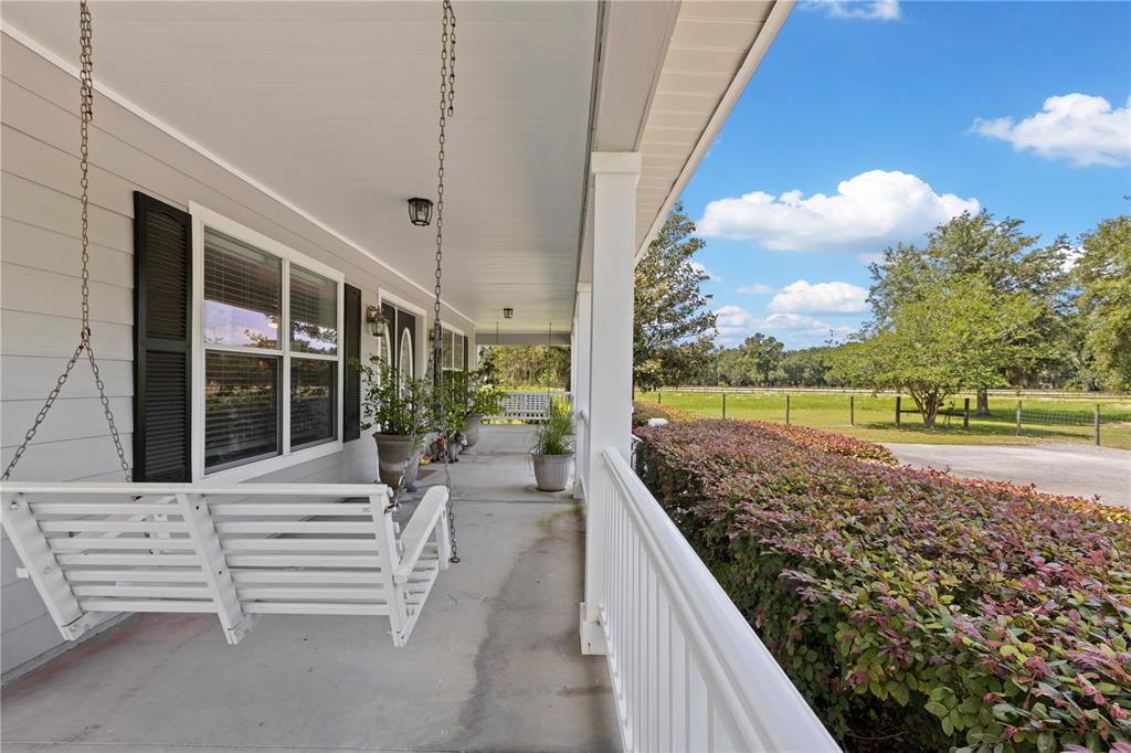 A covered porch features a white hanging swing, white railings, and a view of a yard — 9897 NW 160 AVENUE, MORRISTON, FL