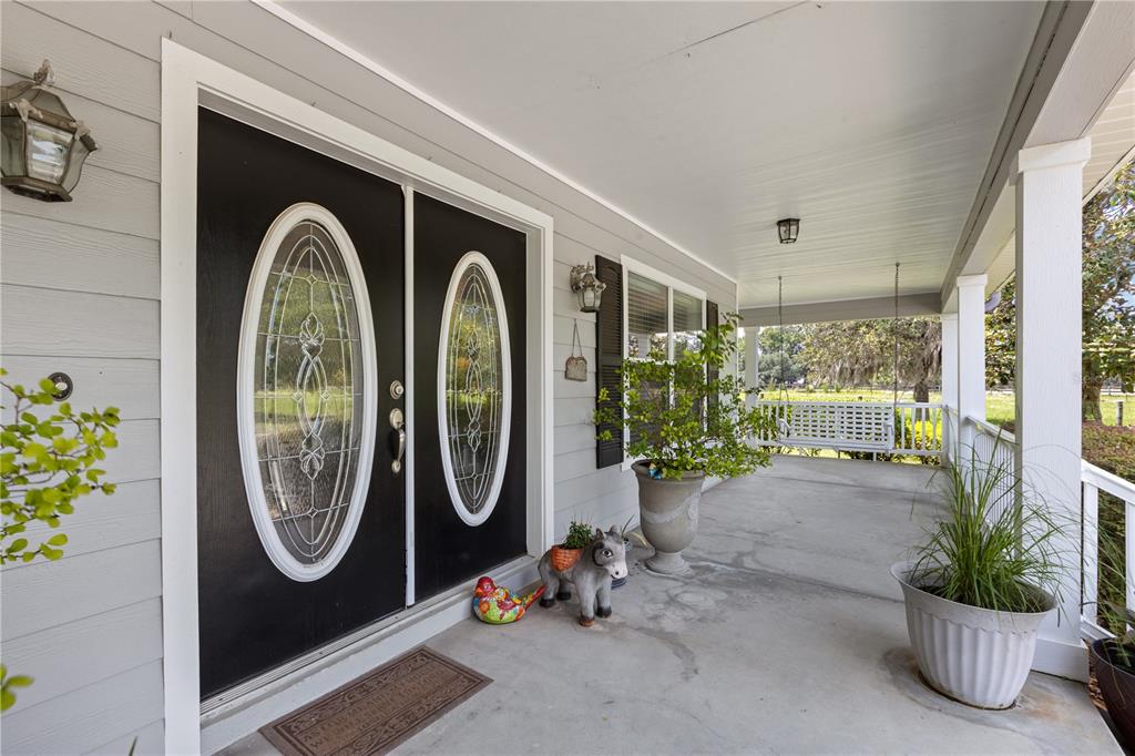 A covered front porch features a black double door with oval glass inserts and potted plants — 9897 NW 160 AVENUE, MORRISTON, FL