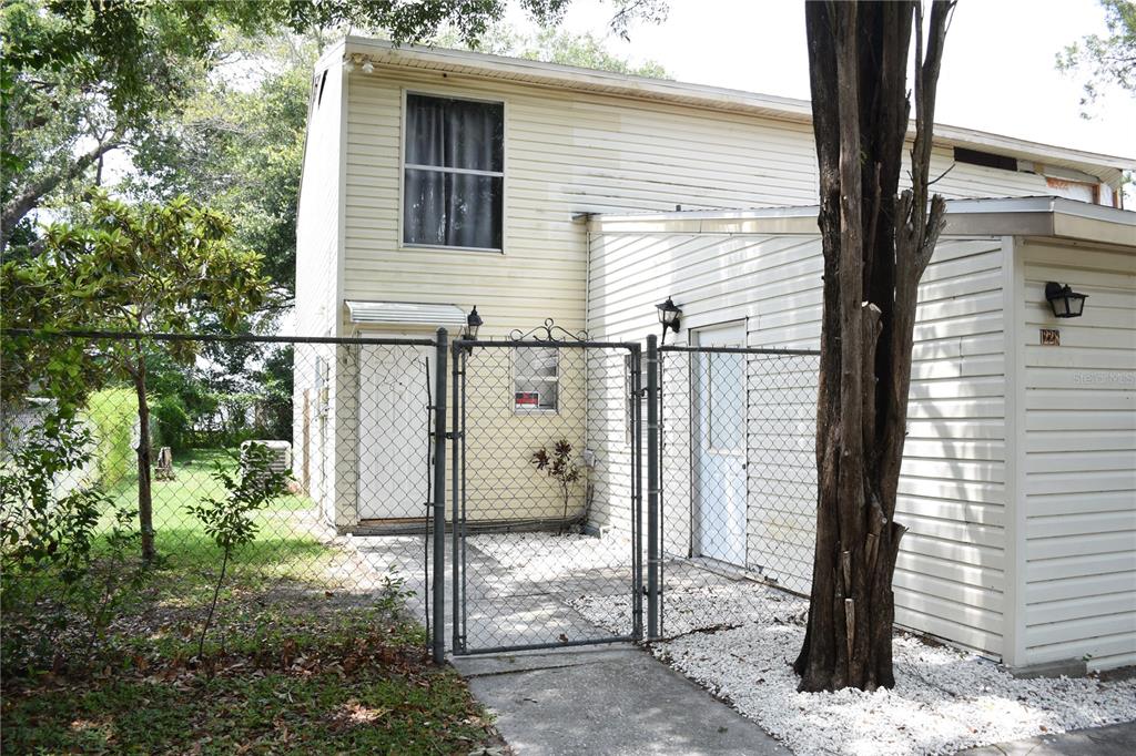 A two-story house exterior features light-colored siding, a chain-link fence, and a gated entrance — 1228 GOLCONDA ROAD, LAKELAND, FL