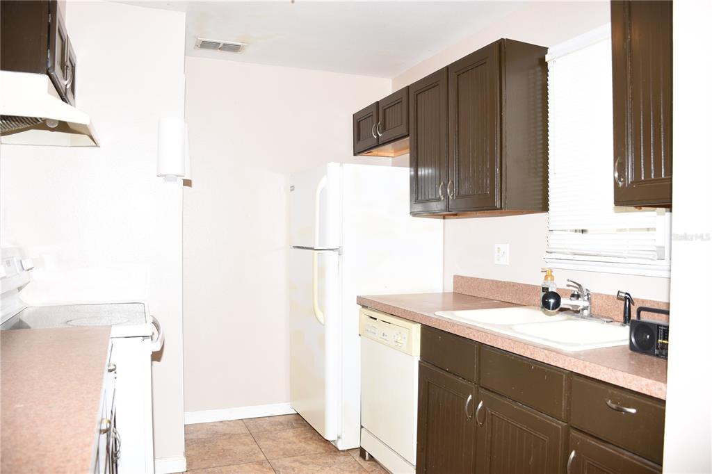 A kitchen features dark brown cabinets, white appliances, a double sink, and tiled flooring — 1228 GOLCONDA ROAD, LAKELAND, FL