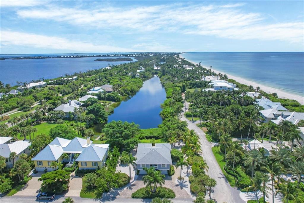 An aerial view shows a coastal neighborhood with houses surrounding a central pond and beach — 4010 40TH STREET W, BOCA GRANDE, FL