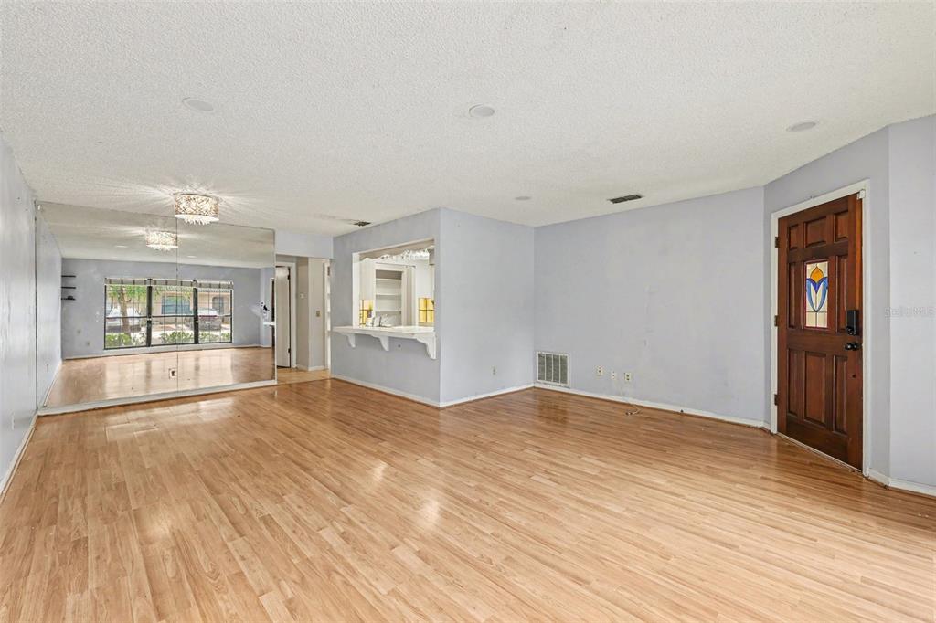An empty living room features light wood flooring, a mirrored wall, and a breakfast bar — 1916 SW 34TH COURT, OCALA, FL