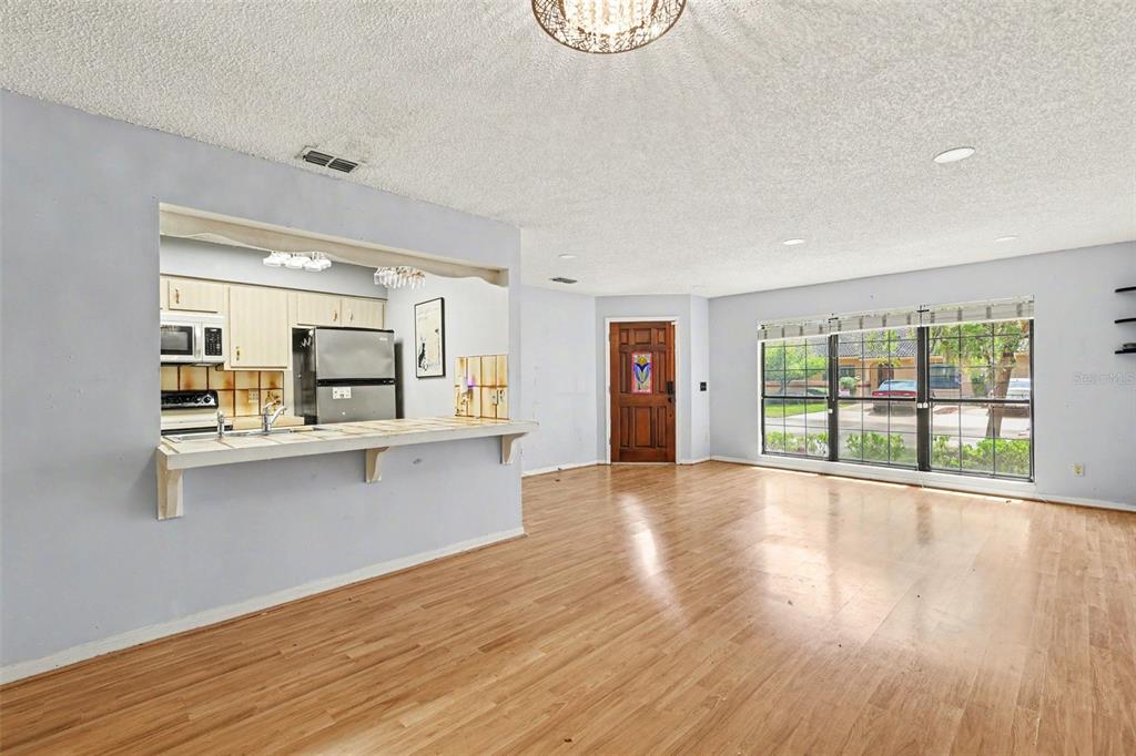 A living room with light wood flooring, a kitchen pass-through window, and a front door — 1916 SW 34TH COURT, OCALA, FL