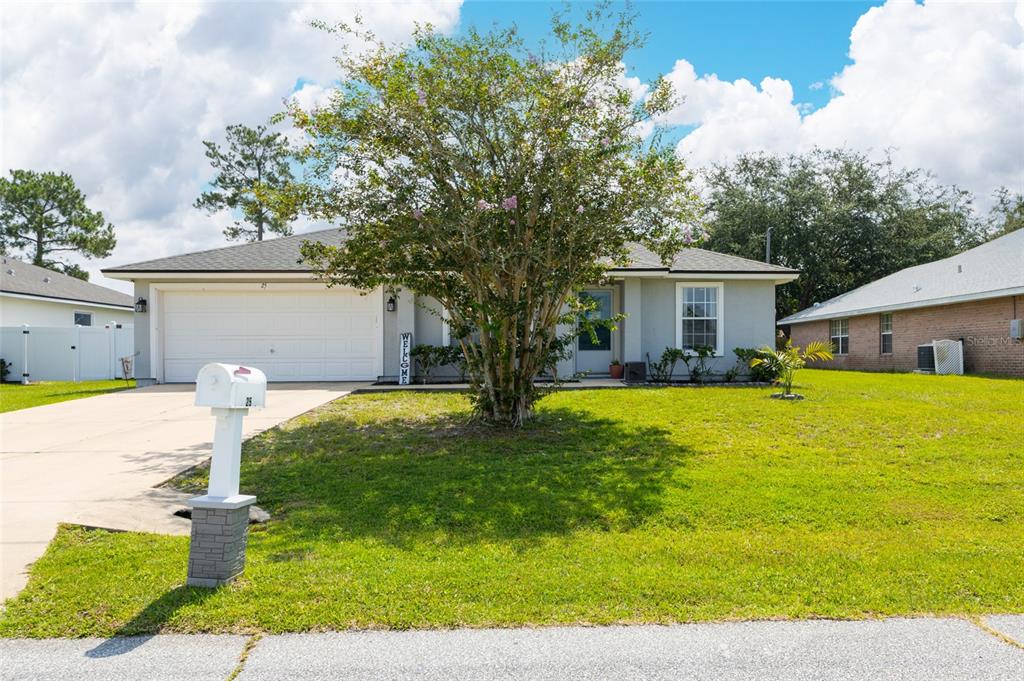 A single-story house with a white garage, a large tree, and a mailbox in front — 25 ROCKINGHAM LANE, PALM COAST, FL