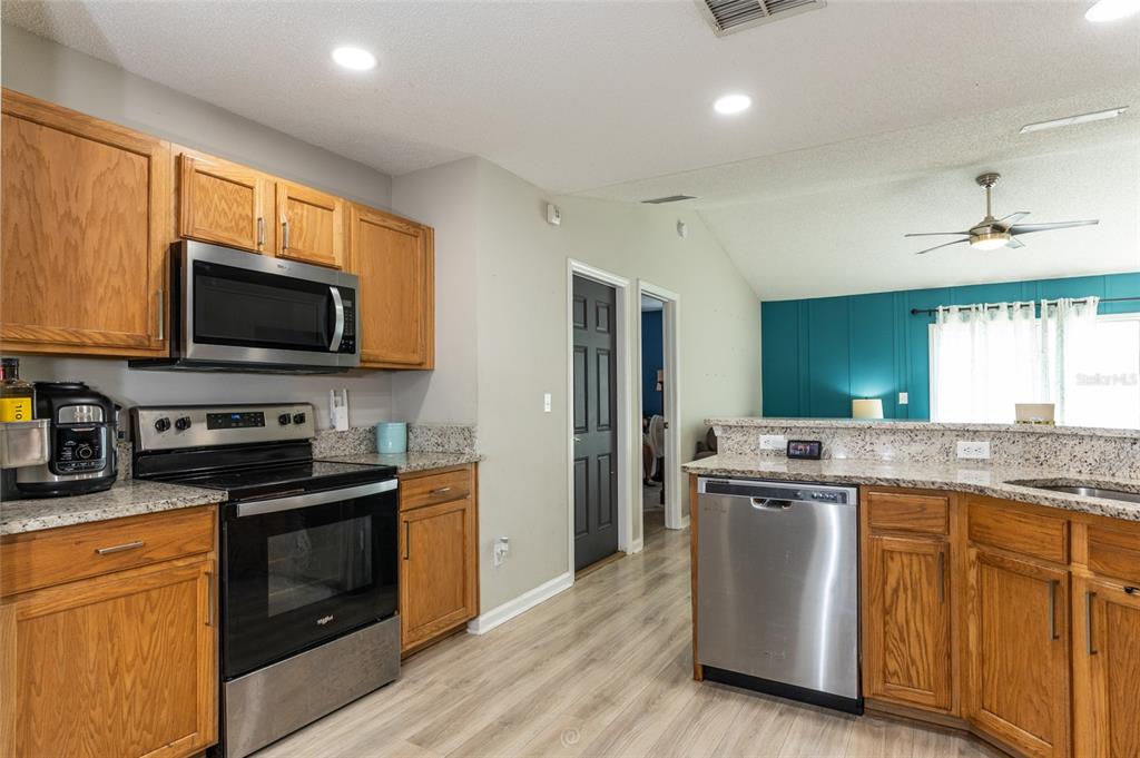 A kitchen features wood cabinets, granite countertops, stainless steel appliances, and light wood flooring — 25 ROCKINGHAM LANE, PALM COAST, FL