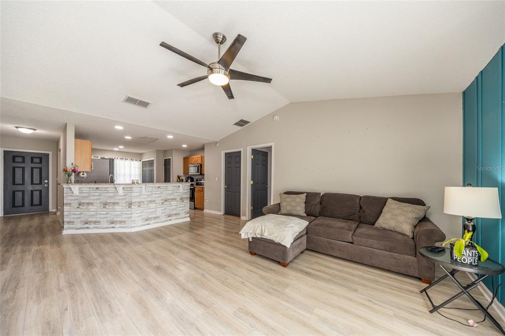 A living room with light wood-look flooring, a gray sectional sofa, and a kitchen peninsula — 25 ROCKINGHAM LANE, PALM COAST, FL