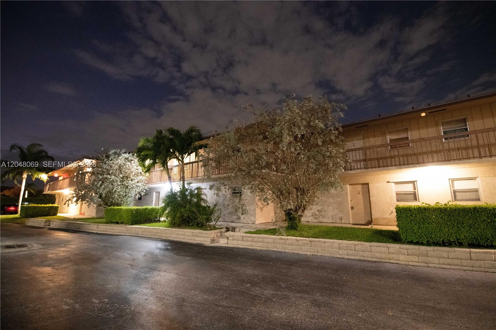 A two-story apartment building exterior at night with palm trees and a low stone wall — 2755 W Atlantic Ave # 105A, Delray Beach FL 33445, DELRAY BEACH, FL