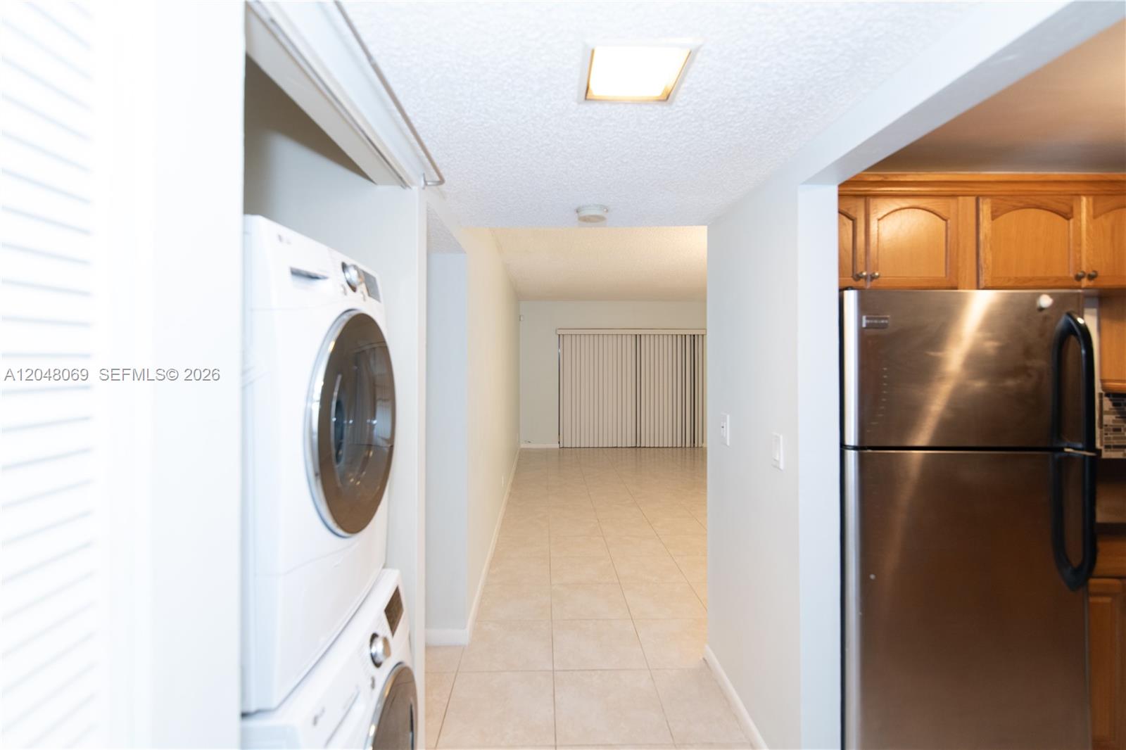 A hallway connects a laundry closet with a stacked washer-dryer to a kitchen and living area — 2755 W Atlantic Ave # 105A, Delray Beach FL 33445, DELRAY BEACH, FL