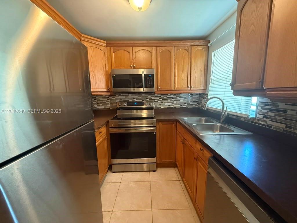 A kitchen features wood cabinets, stainless steel appliances, a tiled backsplash, and dark countertops — 2755 W Atlantic Ave # 105A, Delray Beach FL 33445, DELRAY BEACH, FL