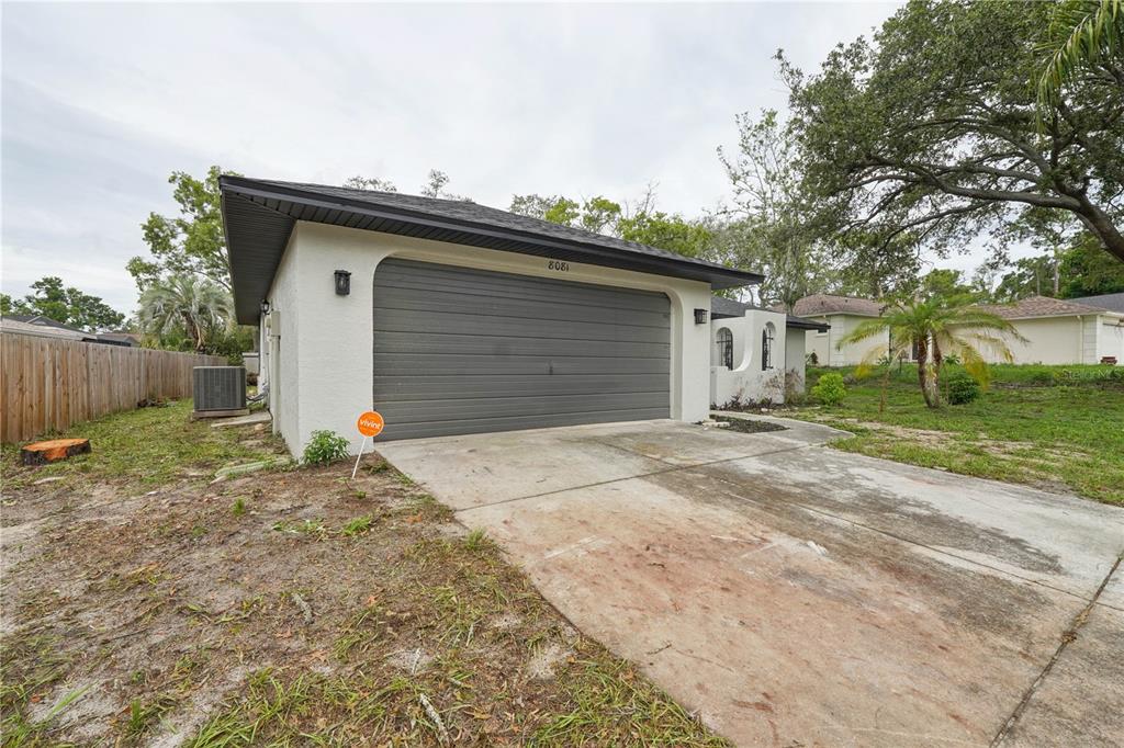 A single-story house exterior features a two-car garage, a concrete driveway, and a fenced yard — 8081 WOODEN DRIVE, SPRING HILL, FL