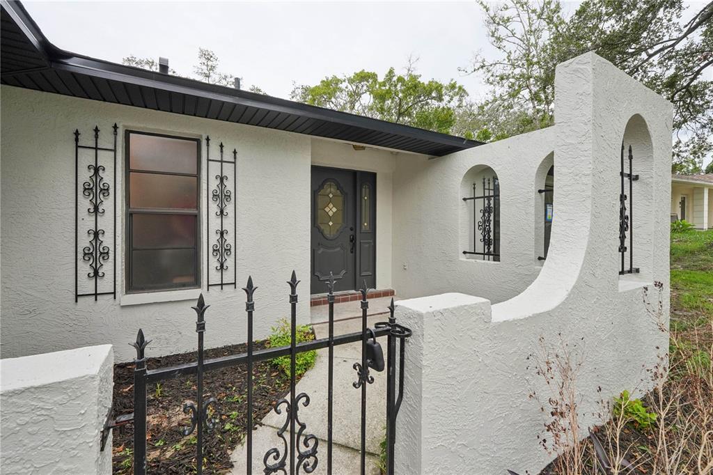 A white stucco house exterior features a gated courtyard, arched openings, and black iron accents — 8081 WOODEN DRIVE, SPRING HILL, FL