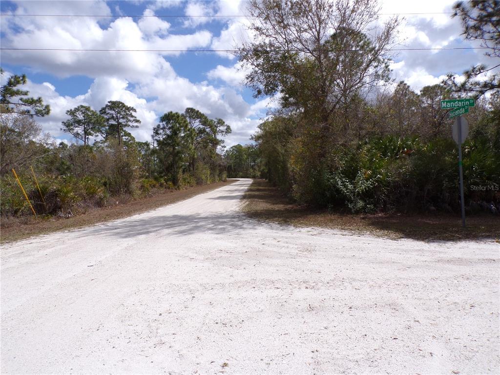 A dirt road stretches into a wooded area with a street sign on the right — 27263 HACIENDA DRIVE, PUNTA GORDA, FL