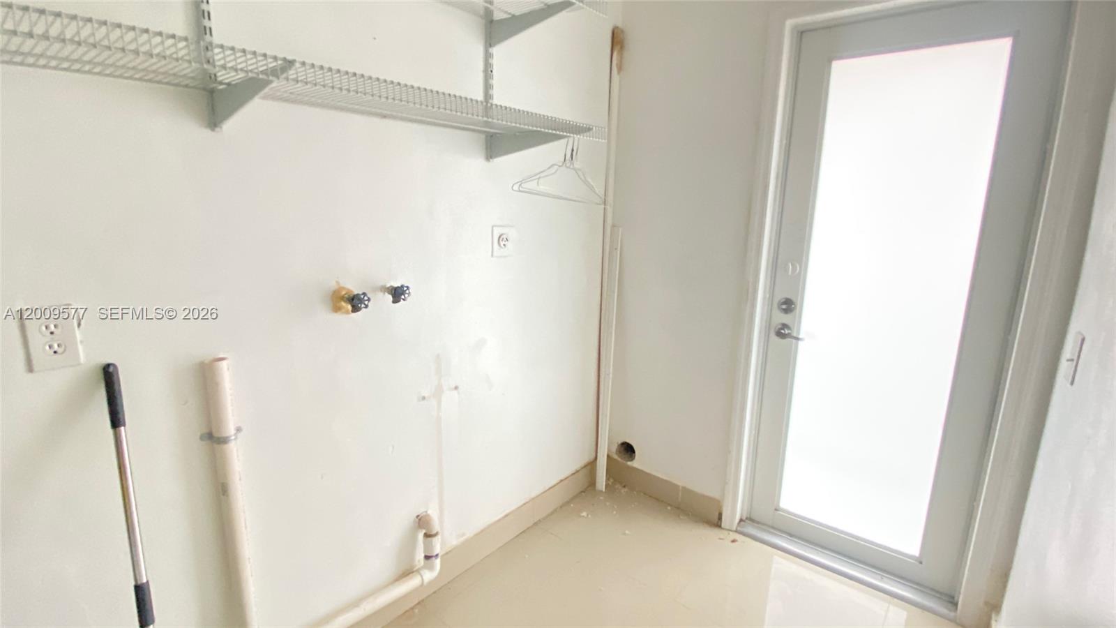 This laundry room features white walls, wire shelving, plumbing hookups, and a glass-paneled door — 530 NW 99th St, Miami FL 33150, MIAMI, FL