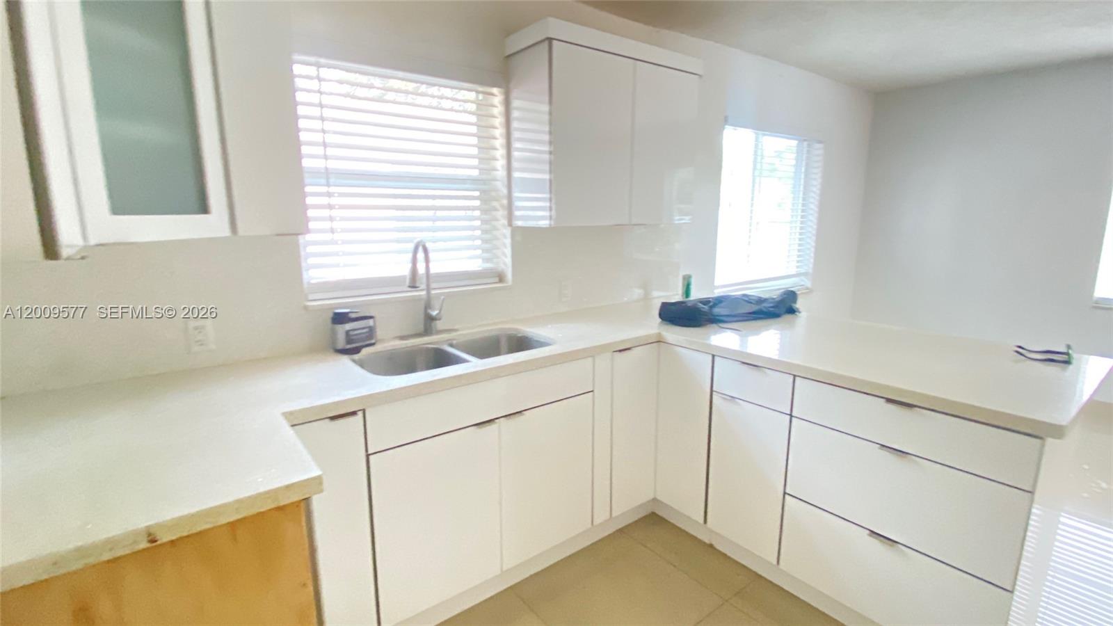 A kitchen features white cabinets, light countertops, a double sink, and a window with blinds — 530 NW 99th St, Miami FL 33150, MIAMI, FL