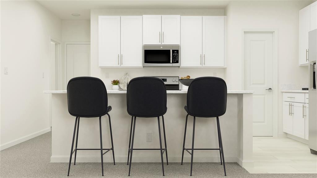 A kitchen island with three black bar stools faces white cabinets and a built-in microwave — 10162 ELDERFLOWER DRIVE, DADE CITY, FL