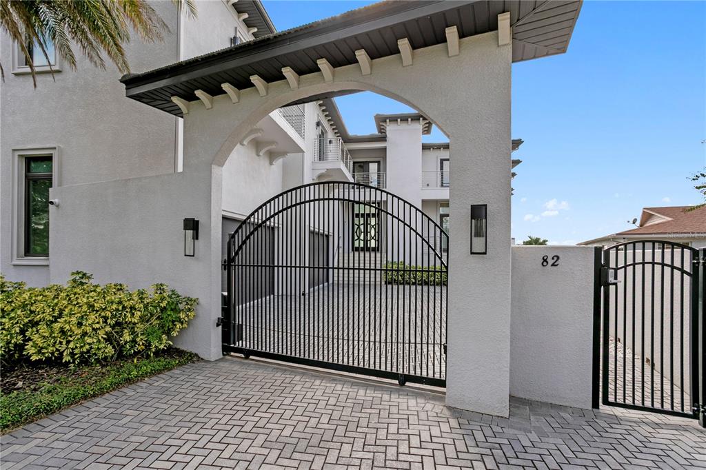 A white stucco arched entryway features a black metal gate and a paved driveway — 82 MARTINIQUE AVENUE, TAMPA, FL