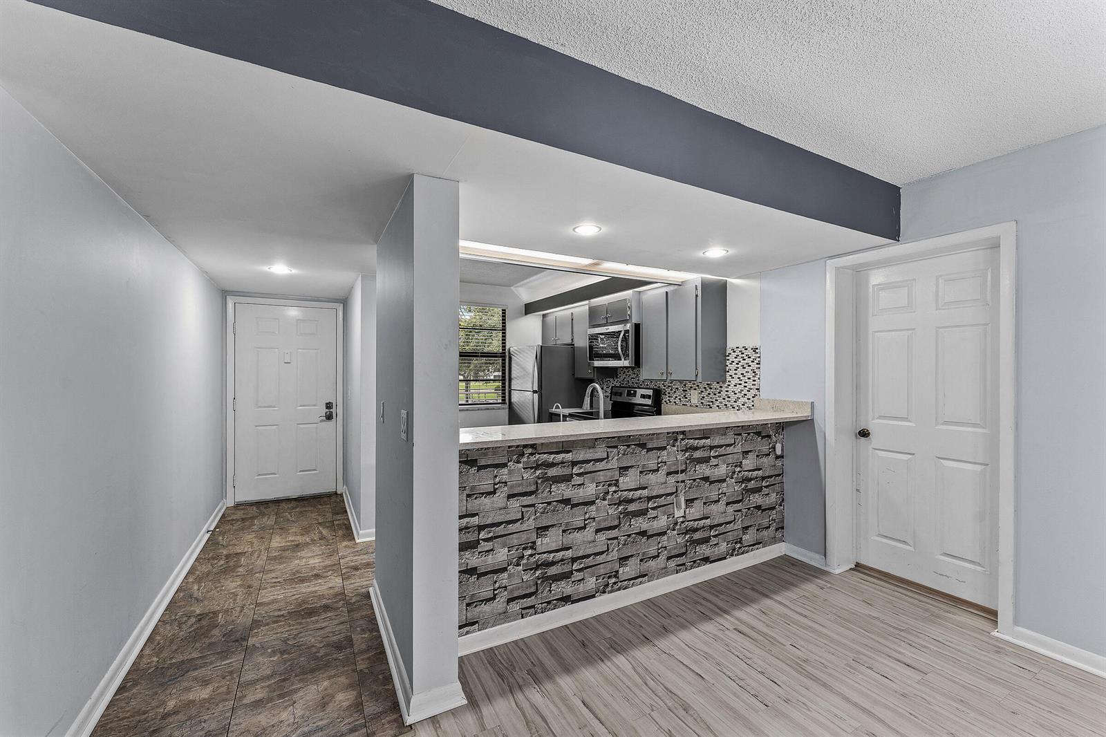 A view of a kitchen with a stone-accented breakfast bar, tile flooring, and white doors — 6097 Balboa Circle # 202, Boca Raton FL 33433, BOCA RATON, FL