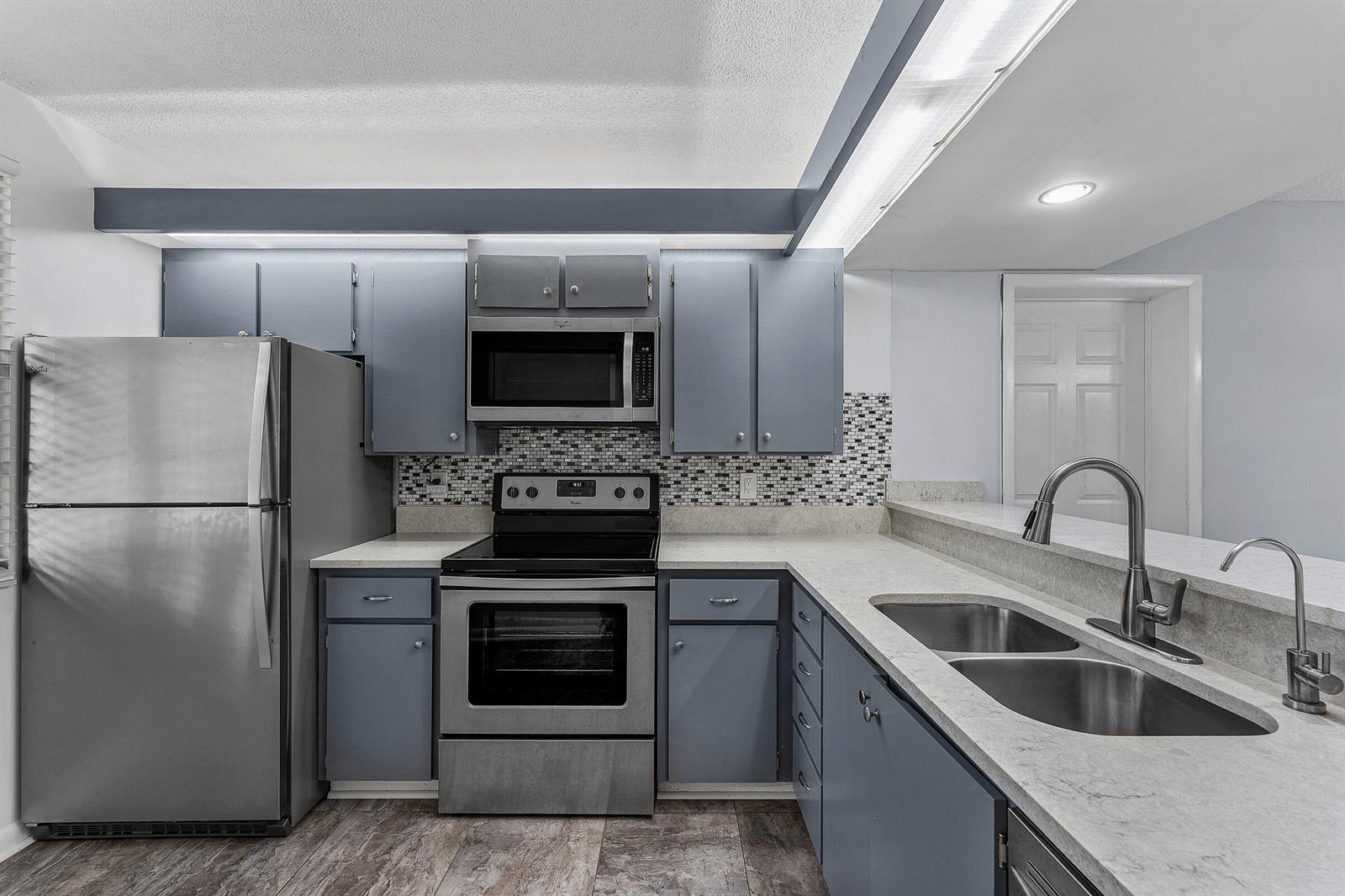 A kitchen features blue cabinets, stainless steel appliances, a mosaic backsplash, and light countertops — 6097 Balboa Circle # 202, Boca Raton FL 33433, BOCA RATON, FL
