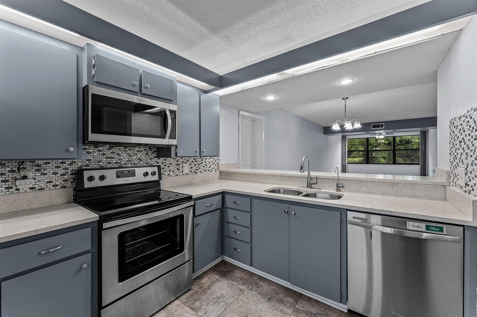 A kitchen with blue cabinets, stainless steel appliances, and a pass-through window to the living area — 6097 Balboa Circle # 202, Boca Raton FL 33433, BOCA RATON, FL
