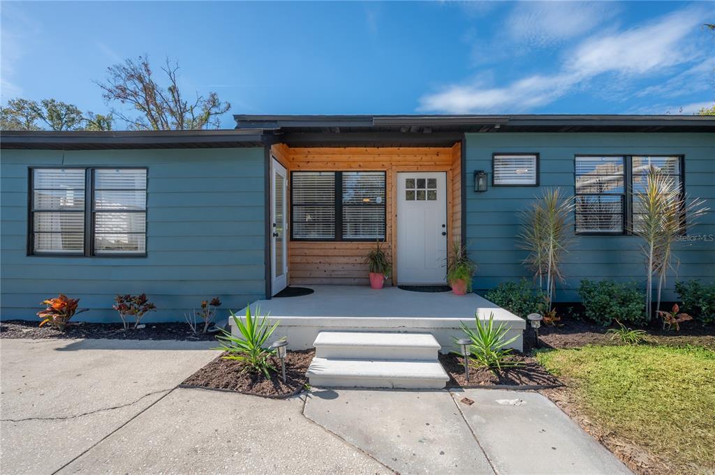 A blue house exterior features a concrete porch with steps and natural wood siding accents — 4110 N MARGUERITE STREET, TAMPA, FL