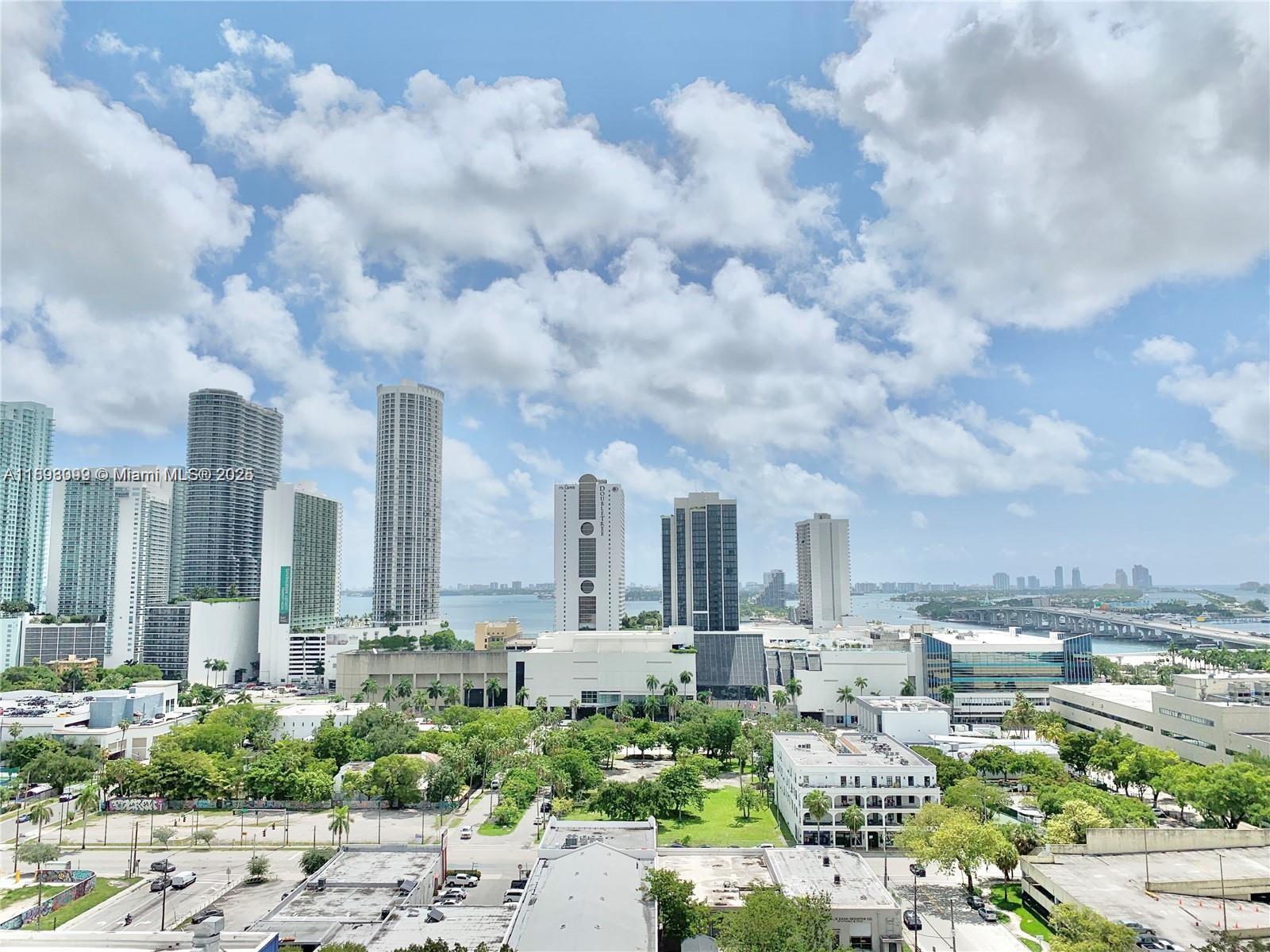 An elevated view of a city skyline with high-rise buildings, trees, and a distant bridge — 1600 NE 1st Ave # 1003, Miami FL 33132, MIAMI, FL