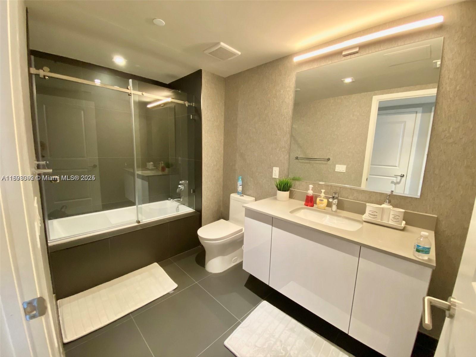 A modern bathroom features a glass-enclosed tub, a white vanity, and gray tiled flooring — 1600 NE 1st Ave # 1003, Miami FL 33132, MIAMI, FL