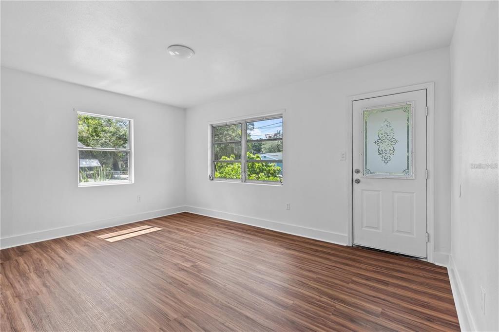 A bright, empty room features white walls, wood-look flooring, two windows, and a front door — 2314 N OSPREY AVENUE, SARASOTA, FL